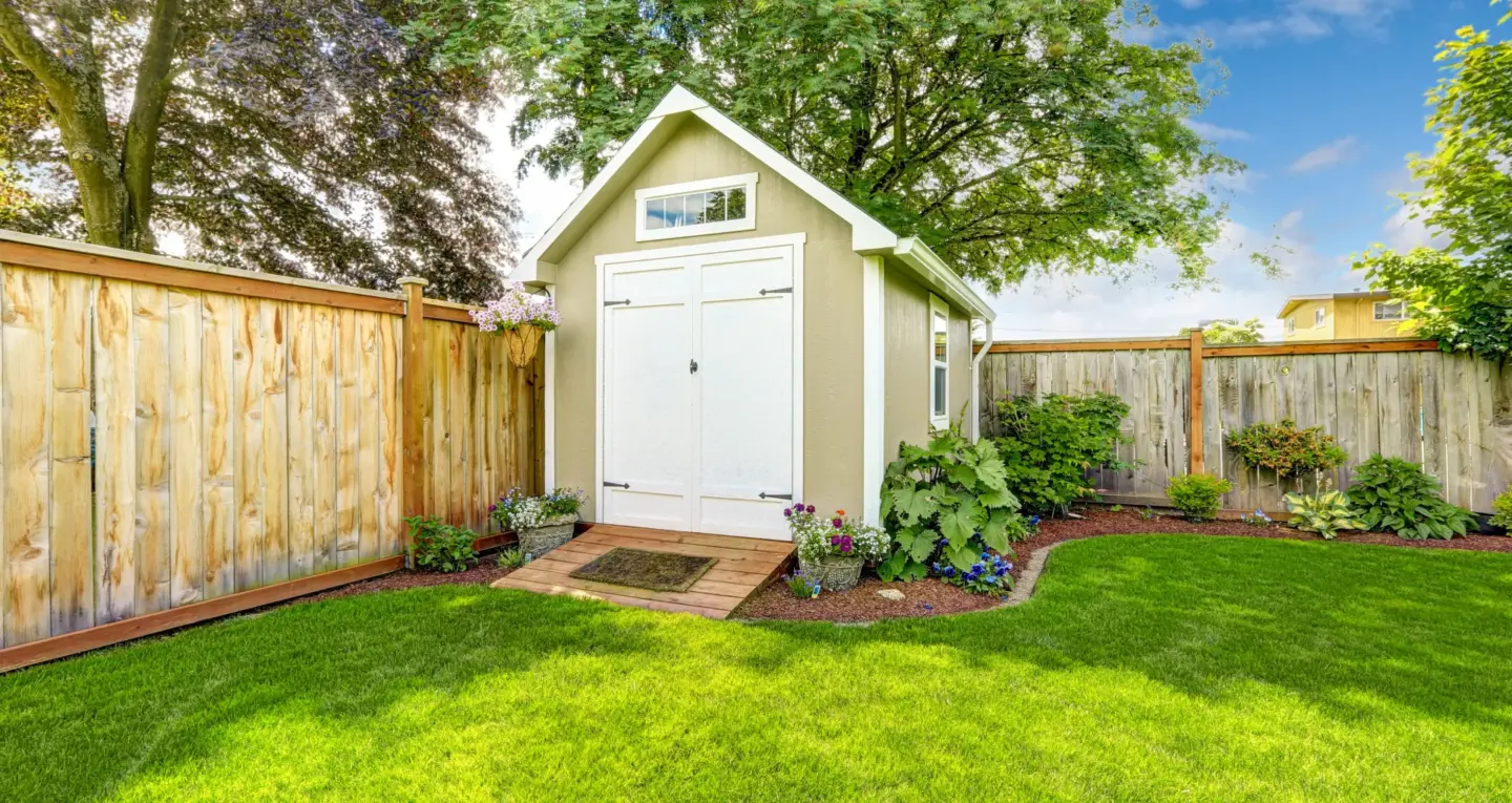 backyard-mocha-shed-with-white-door-surrounded-by-plants-decorations-and-wooden-wall-privacy-fence-in-southern-maryland