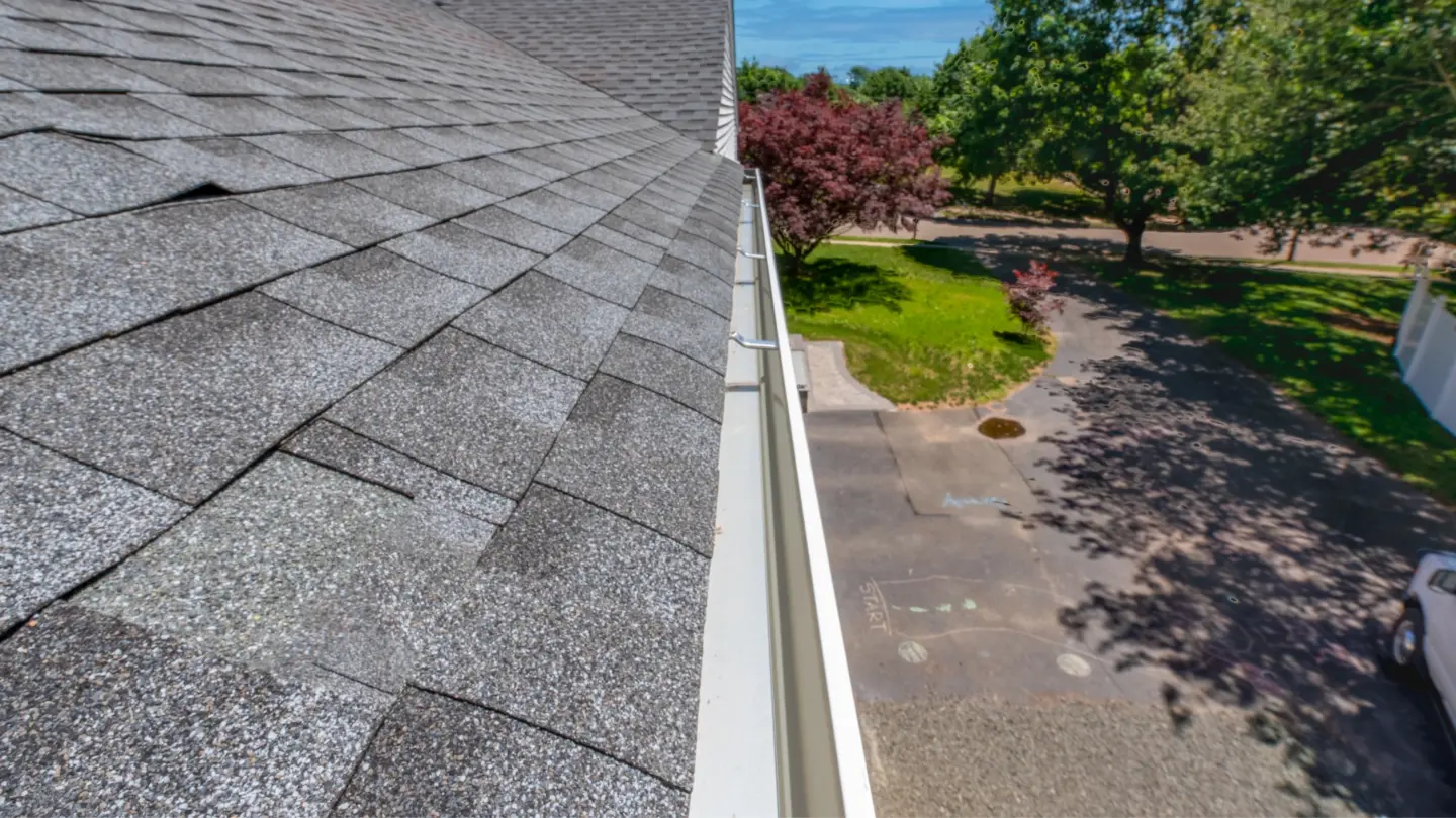gutter-installation-on-the-gray-roof-top-with-car-grass-plants-and-trees-on-the-background-in-huntingtown-maryland