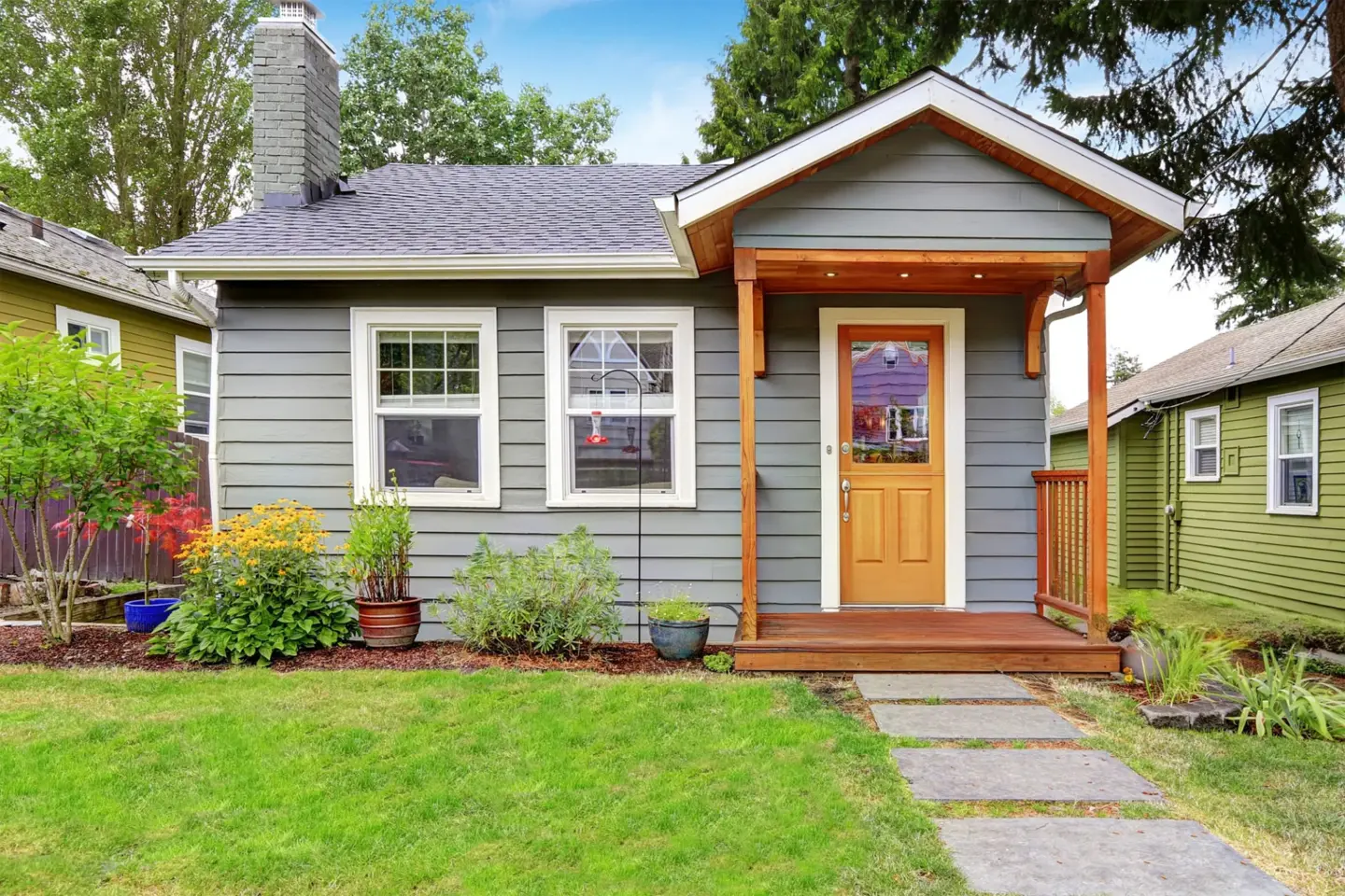 small-american-house-with-gray-exterior-paint-porch-surrounded-by-plants-grass-and-residential-house-on-the-background-in-southern-maryland